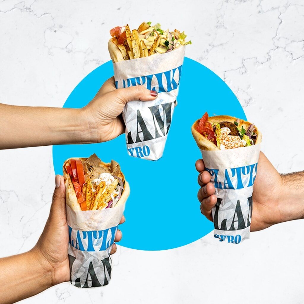 Two Nick the Greek gyros held up against blue
